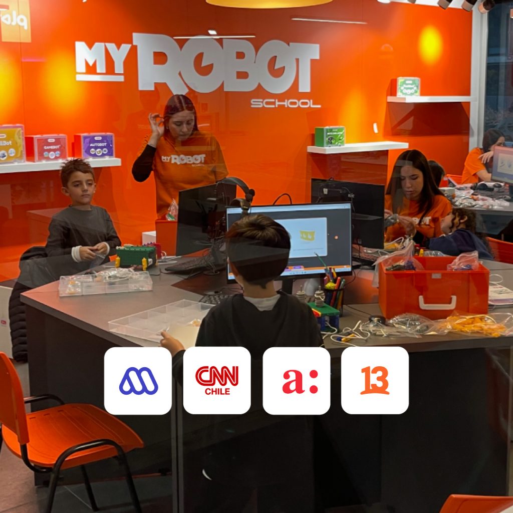 Aula de My Robot School con niños y niñas armando robots en mesas de trabajo, guiados por instructoras con poleras naranjas corporativas. Al frente, una pantalla de computador muestra un diseño 3D. En la parte inferior se ven los logotipos de Mega, CNN Chile, Agricultura y Canal 13C.